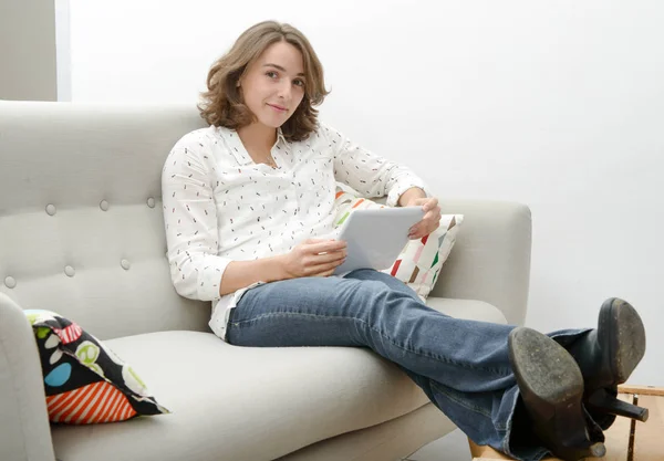 Hermosa mujer joven con una tableta en el sofá — Foto de Stock