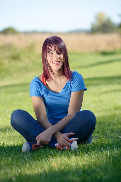 Schöne junge Frau sitzt im Gras — Stockfoto