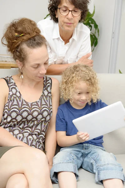 Child and his mother with grandmother play with tablet — Stock Photo, Image