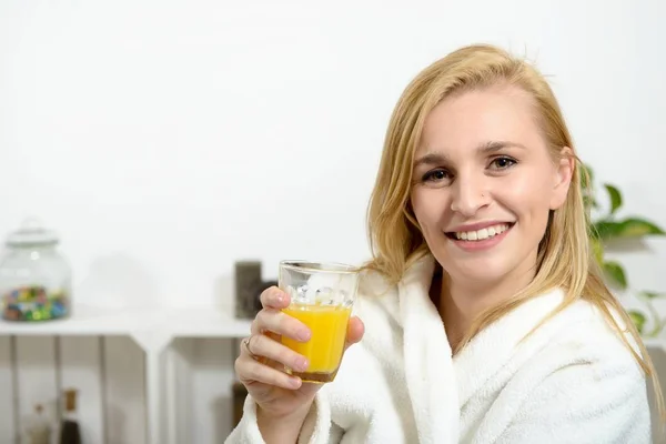 Schöne junge blonde Frau trinkt Orangensaft — Stockfoto