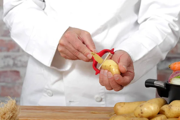 Mani di un uomo pelare la patata con pelapatate — Foto Stock