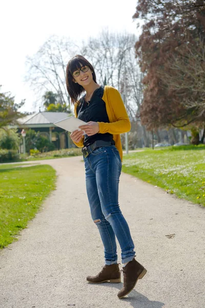 Young brunette girl with a tablet in park, outside — Stock Photo, Image