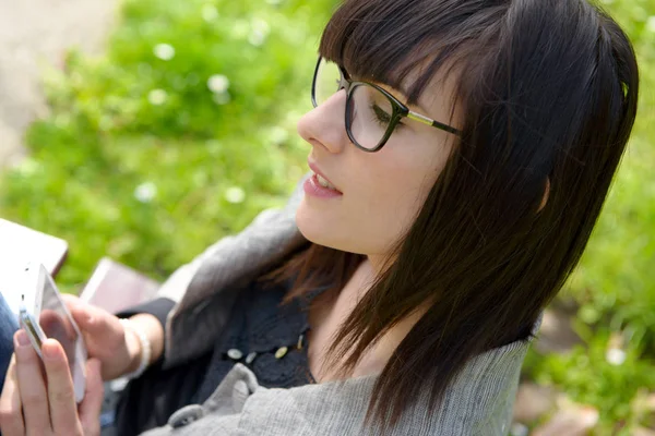 Junges brünettes Mädchen mit einem Handy im Park, draußen — Stockfoto