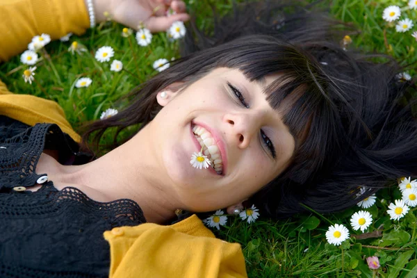 Junge brünette Frau liegt mit Gänseblümchen im Gras — Stockfoto