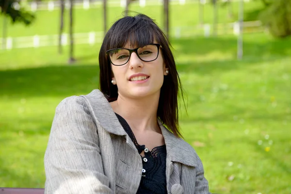 Mujer joven con chaqueta gris y gafas en el parque — Foto de Stock