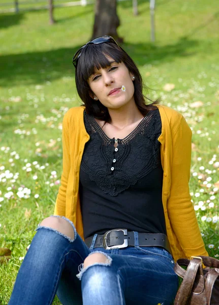 屋外の公園で芝生の上に座っている若いブルネットの少女 — ストック写真