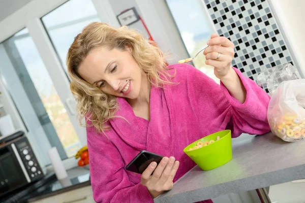 Jonge blonde vrouw eten granen en telefoon in de ochtend — Stockfoto
