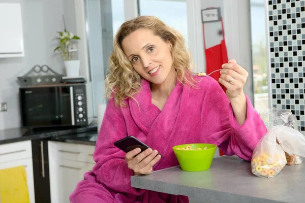 Jovem loira comendo cereais e telefone pela manhã — Fotografia de Stock