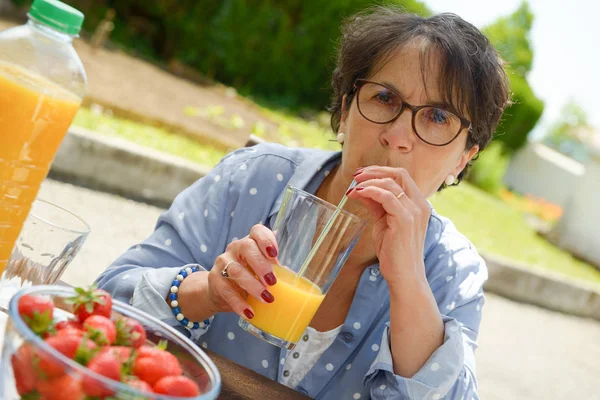 Senior vrouw drinken sinaasappelsap in haar tuin — Stockfoto