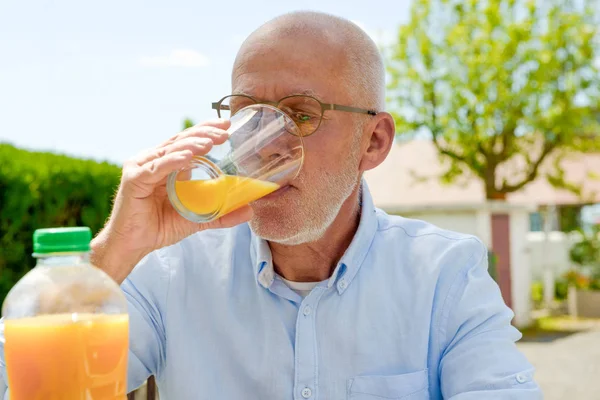 Senior homme boire du jus d'orange dans son jardin — Photo