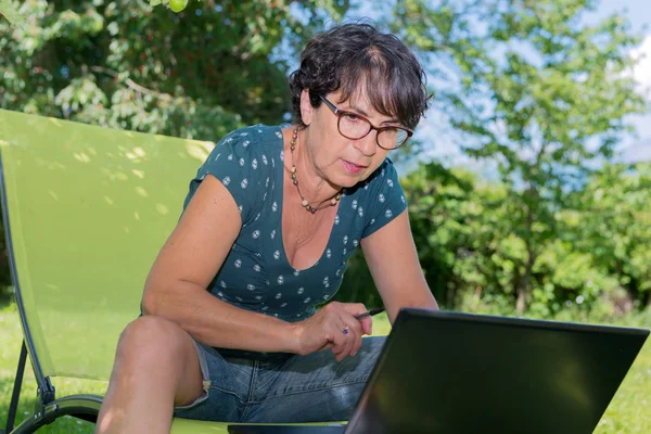 Modern casual woman sitting at garden with laptop — Stock Photo, Image