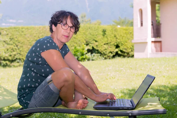 Mujer casual moderna sentada en el jardín con portátil — Foto de Stock