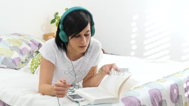 Όμορφη νεαρή γυναίκα ξαπλωμένη στο κρεβάτι Ακούστε μουσική με τα ακουστικά — Αρχείο Βίντεο