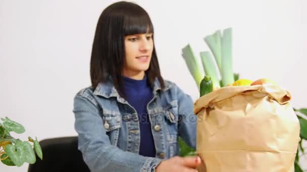 Jonge brunette vrouw met een boodschappentas vol groenten eet een appel — Stockvideo