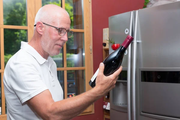 Homem maduro com garrafa de vinho tinto, na cozinha — Fotografia de Stock