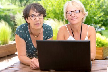 bahçe terasında, dizüstü bilgisayar kullanarak iki Olgun kadın arkadaş