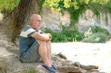 bir ağacın altında oturan olgun kel adam