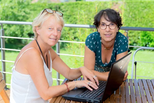 Két érett nők barátok használ a laptop, a kerti teraszon — Stock Fotó