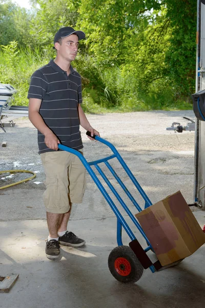 Mladý zaměstnanec nese balíček s handtruck — Stock fotografie