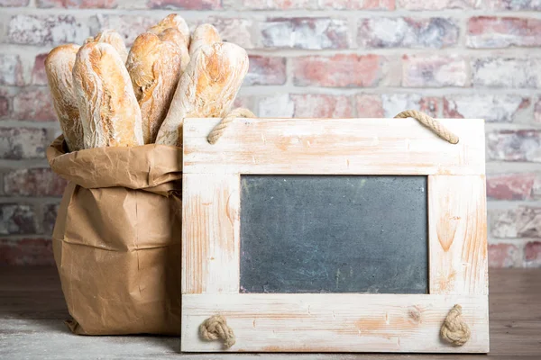 French bread with chalkboard on a rustic table — Stock Photo, Image