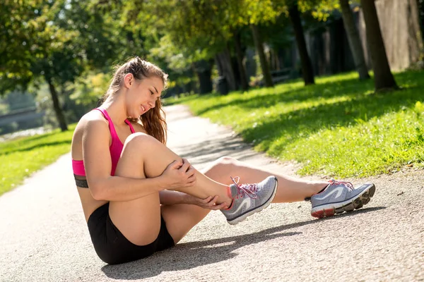 Genç bayan koşucu dışarıda acı içinde ayağa dokunuyor.