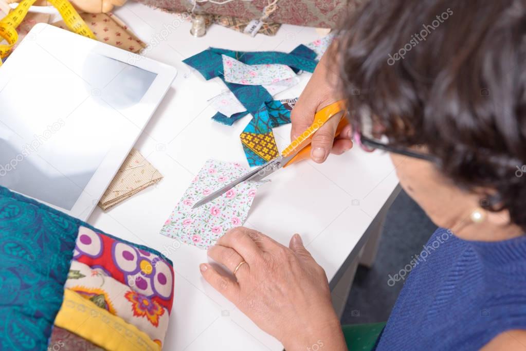 mature brunette woman cutting fabric for sewing patchwork