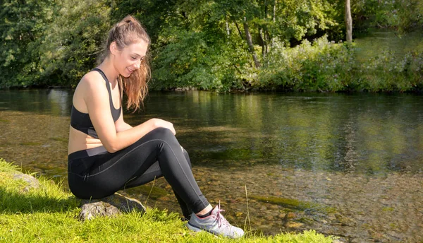Docela sportovní dívka relaxaci a posezení u řeky — Stock fotografie
