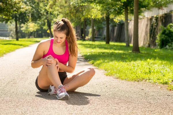 Young woman runner touching knee in pain outdoors — Stock Photo, Image