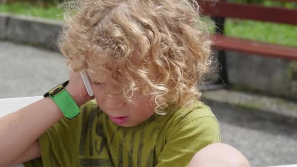 Pequeño chico rubio jugando con un teléfono inteligente — Vídeo de stock