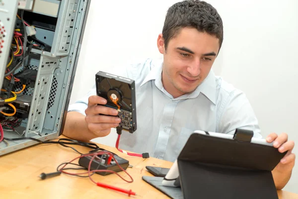 Mladý technik, který pracuje na nefunkční počítač s tabletem — Stock fotografie