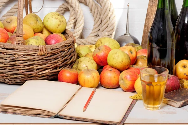 Basket of apples, bottles of cider and old notebook — Stock Photo, Image