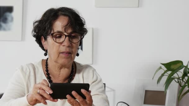 Ανώτερος γυναίκα χρησιμοποιώντας ένα smartphone και χαμογελαστός — Αρχείο Βίντεο