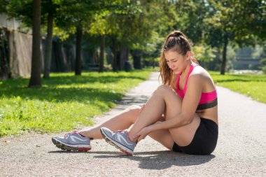Genç bayan koşucu dışarıda acı içinde ayağa dokunuyor.