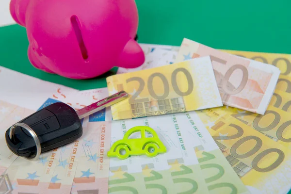 Banco piggy rosa com dinheiro, chave do carro em um tapete verde — Fotografia de Stock