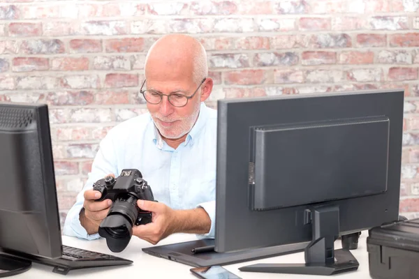 Fotografo che guarda una fotocamera in ufficio con il computer — Foto Stock