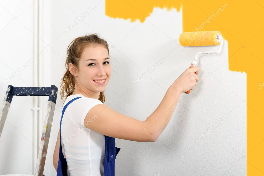 pretty young woman paints the wall yellow color