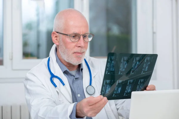Volwassen arts kijken naar een röntgenfoto in een kantoor — Stockfoto