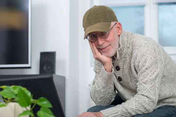 Senior man with cap using laptop at home — Stock Photo, Image