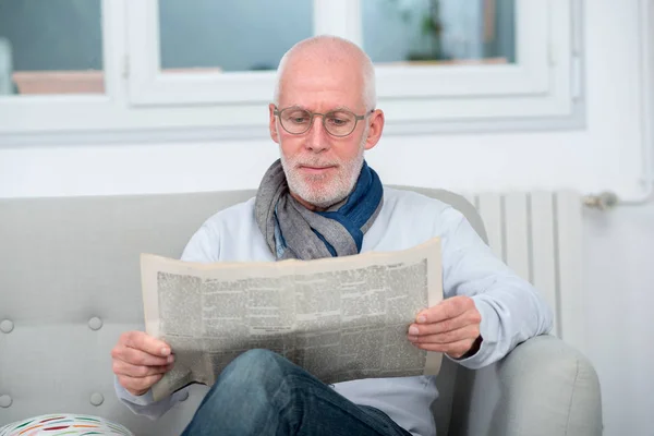 Bonito maduro homem leitura newpaper no sofá — Fotografia de Stock