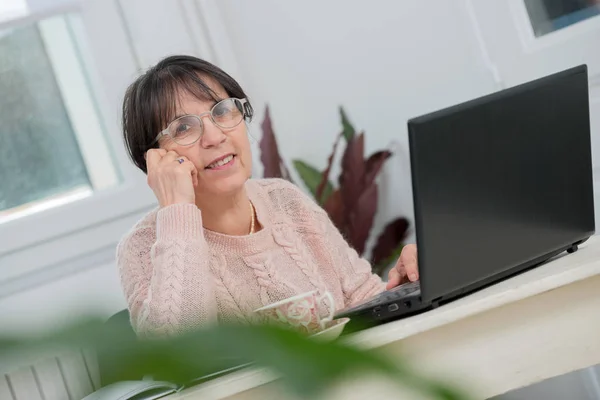 Hermosa mujer de mediana edad utilizando el ordenador portátil en casa —  Fotos de Stock