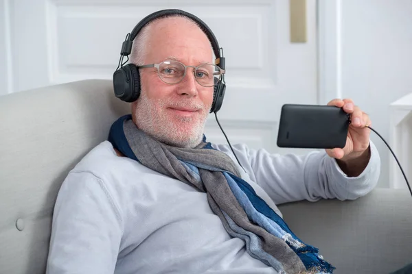 Homem idoso em fones de ouvido ouvindo música em casa — Fotografia de Stock