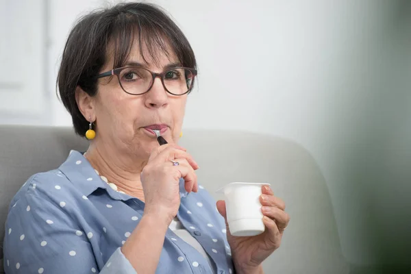 Pretty mature woman eating yogurt at home — Stock Photo, Image
