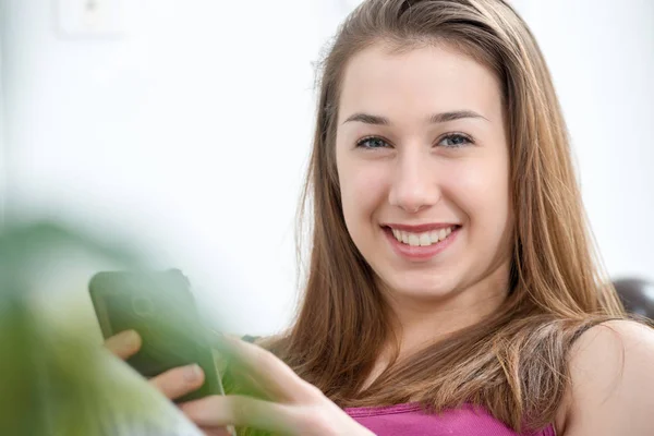 Mujer joven y sonriente usando teléfono inteligente en casa —  Fotos de Stock