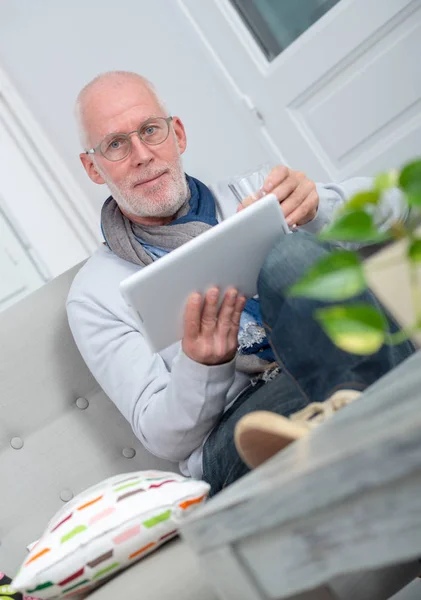 Dojrzały człowiek za pomocą cyfrowego tabletu na kanapie w salonie — Zdjęcie stockowe