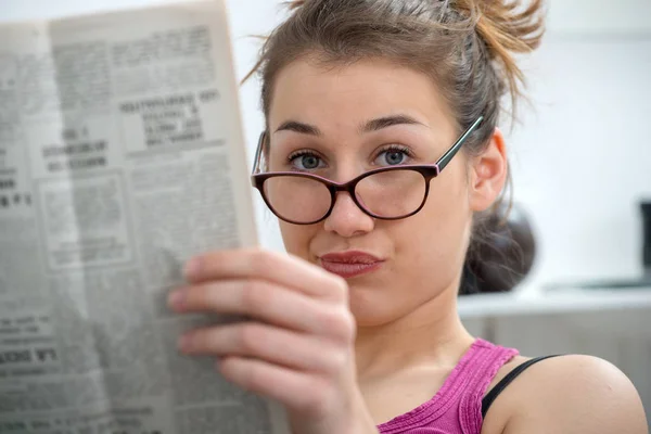 Joven y sonriente mujer con gafas, leyendo el periódico — Foto de Stock