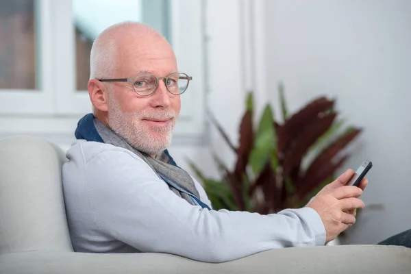 Beau sénior utilisant le téléphone sur le canapé — Photo