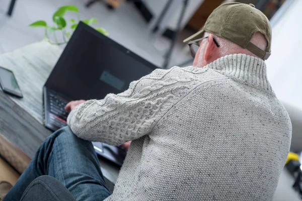 mature man with  baseball cap using a laptop, back view