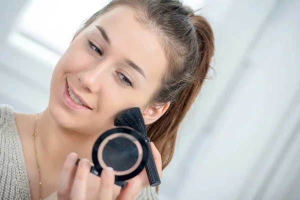 Jovem e sorridente mulher aplicando pó em seu rosto — Fotografia de Stock