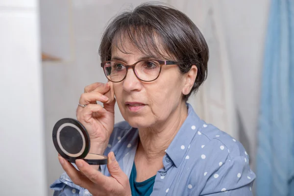 Mature woman doing makeup while looking at small mirror — Stock Photo, Image