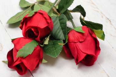 ahşap masa üzerinde üç kırmızı gül